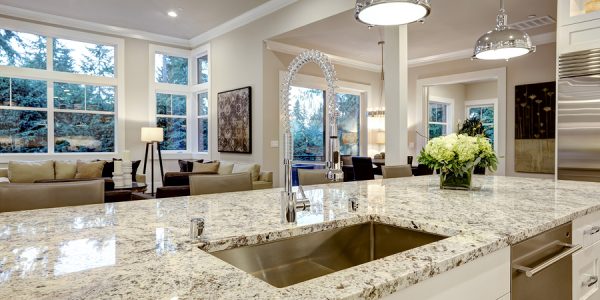 White kitchen design features large bar style kitchen island with granite countertop illuminated by modern pendant lights. Northwest USA